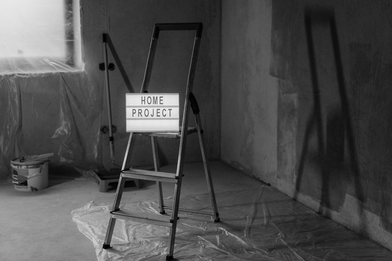 Image en noir et blanc d’un escabeau avec un panneau de projet domestique dans un contexte de rénovation.